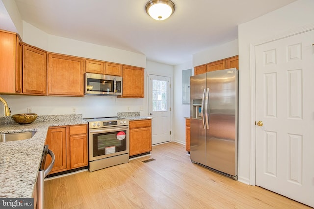 kitchen featuring light stone counters, stainless steel appliances, sink, and light wood-type flooring