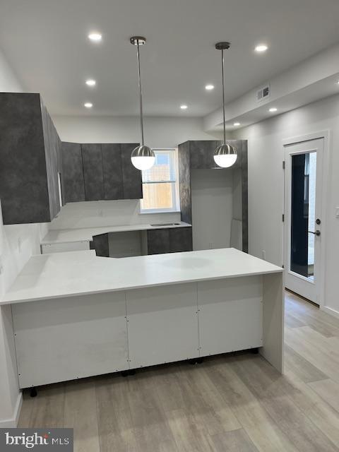 kitchen with kitchen peninsula, light wood-type flooring, and hanging light fixtures