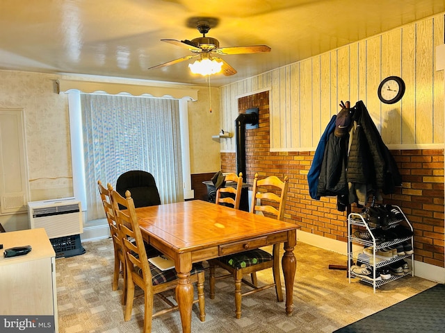 carpeted dining space featuring a wall mounted air conditioner, ceiling fan, wood walls, and brick wall