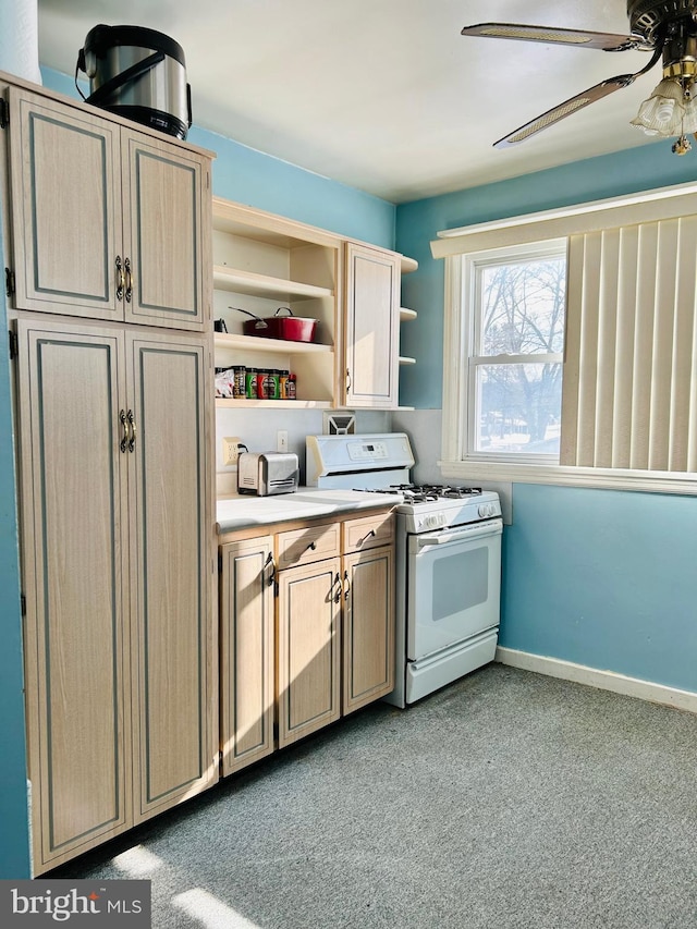 kitchen featuring white range with gas stovetop, light brown cabinetry, light colored carpet, and ceiling fan