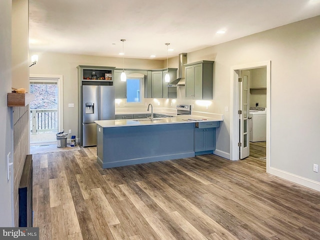 kitchen with pendant lighting, wall chimney exhaust hood, kitchen peninsula, stainless steel appliances, and washer / clothes dryer