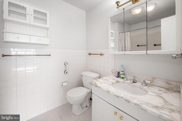 bathroom with tile patterned flooring, toilet, vanity, tile walls, and curtained shower