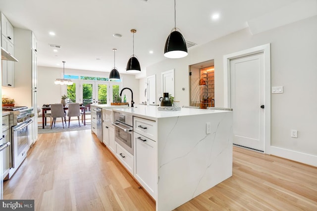 kitchen with pendant lighting, white cabinets, light hardwood / wood-style flooring, gas range, and a large island