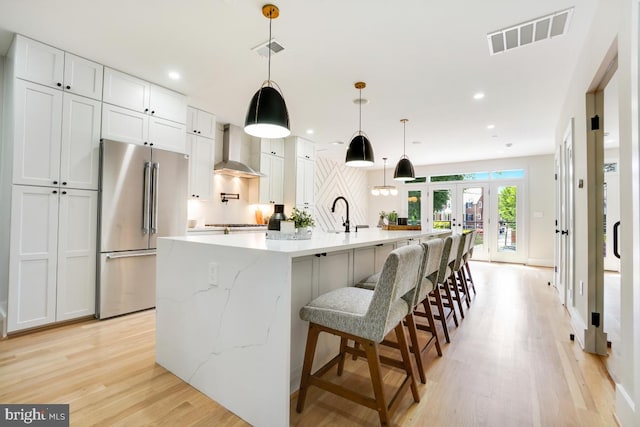 kitchen with white cabinetry, a large island, high end fridge, and wall chimney exhaust hood