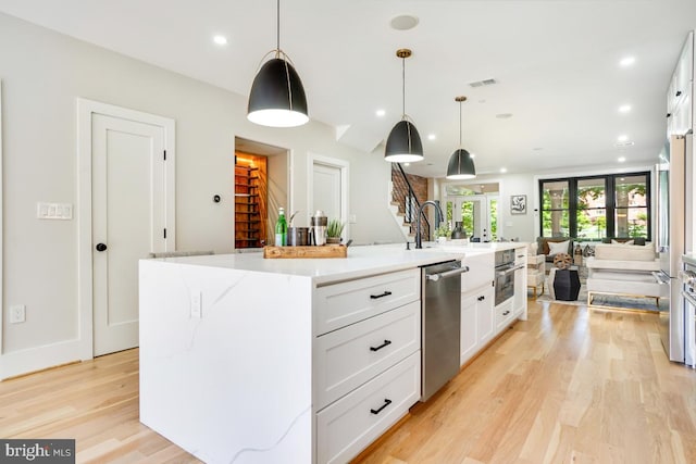 kitchen featuring white cabinetry, an island with sink, light hardwood / wood-style floors, pendant lighting, and appliances with stainless steel finishes