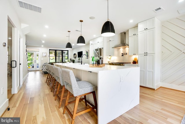 kitchen with a large island, wall chimney exhaust hood, light hardwood / wood-style floors, and white cabinets