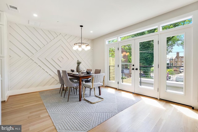 dining space featuring wooden walls, french doors, a notable chandelier, and light wood-type flooring