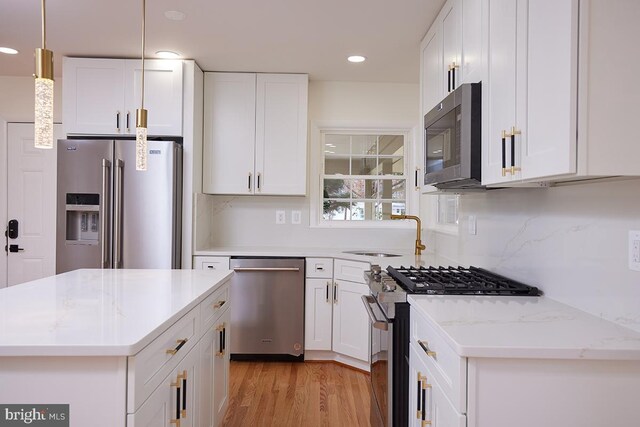 kitchen featuring high quality appliances, white cabinets, sink, hanging light fixtures, and light stone counters