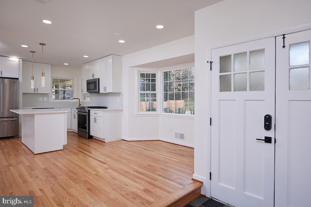 kitchen with white cabinets, decorative light fixtures, a center island, and stainless steel appliances