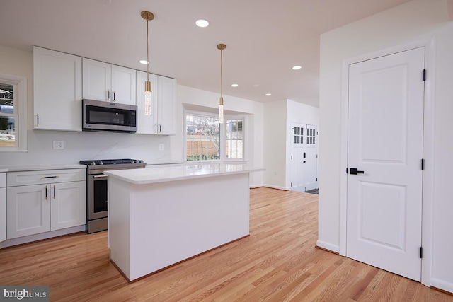 kitchen with appliances with stainless steel finishes, a kitchen island, light hardwood / wood-style floors, white cabinetry, and hanging light fixtures