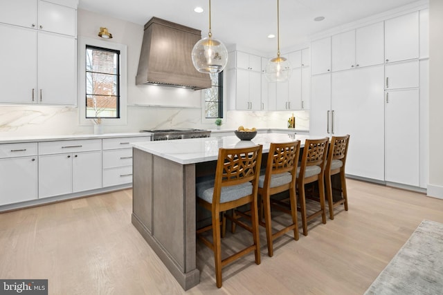 kitchen featuring white cabinets, light wood-style flooring, decorative light fixtures, a center island, and custom exhaust hood