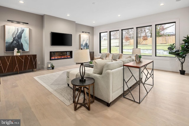 living room with recessed lighting, light wood-style flooring, baseboards, and a glass covered fireplace