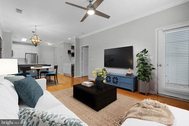 living room with ceiling fan with notable chandelier, light wood-type flooring, and ornamental molding