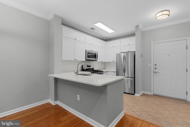 kitchen with kitchen peninsula, appliances with stainless steel finishes, sink, white cabinets, and light hardwood / wood-style floors