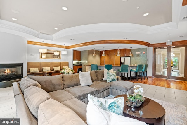 living room with french doors, a tray ceiling, light hardwood / wood-style flooring, and ornamental molding