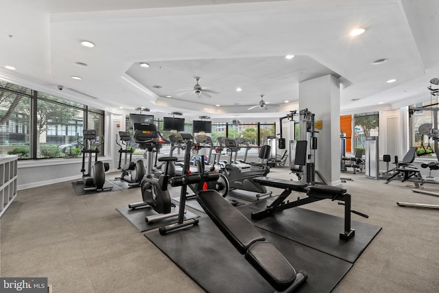 gym featuring a raised ceiling, ceiling fan, a healthy amount of sunlight, and ornamental molding