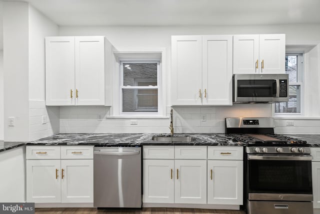 kitchen featuring dark stone countertops, white cabinetry, sink, and stainless steel appliances