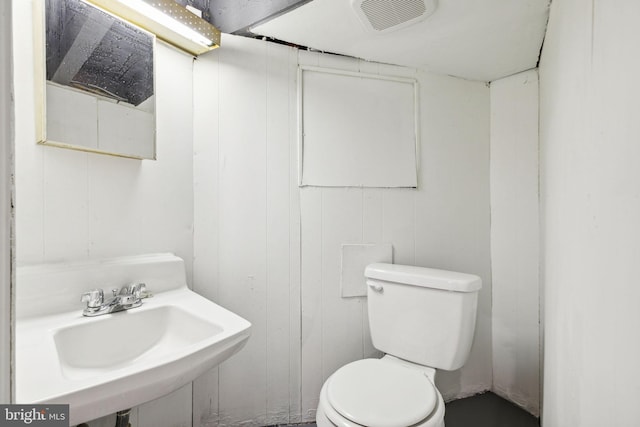 bathroom with wooden walls, sink, and toilet