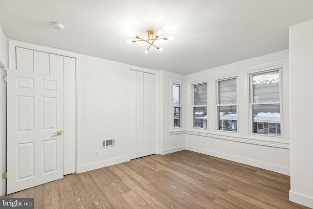 interior space with wood-type flooring, an inviting chandelier, and multiple closets