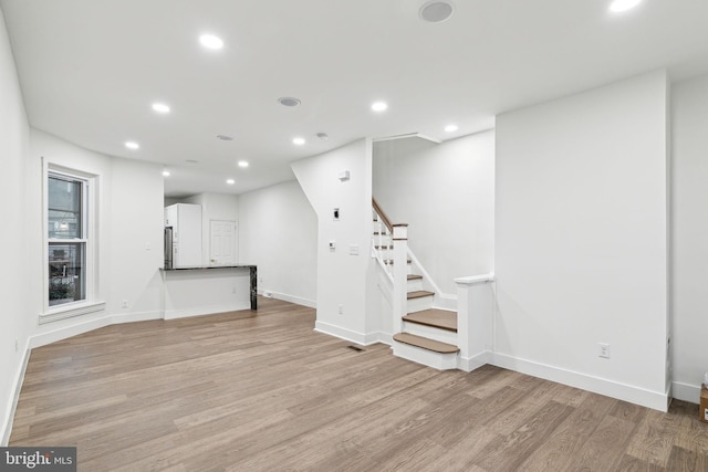 basement with stainless steel fridge and light hardwood / wood-style flooring