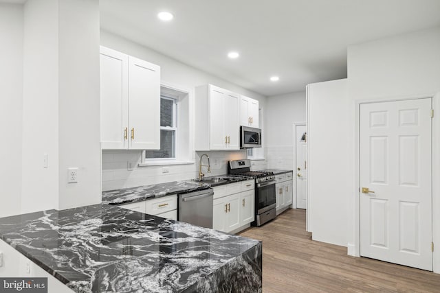 kitchen featuring backsplash, dark stone counters, stainless steel appliances, white cabinets, and light hardwood / wood-style floors