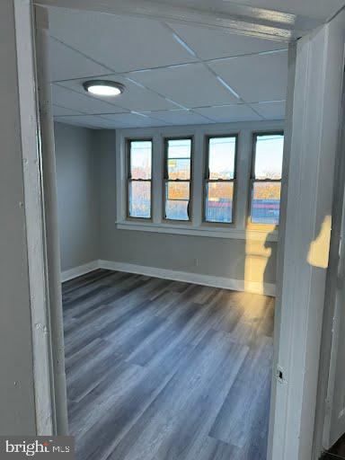 empty room with a drop ceiling, dark hardwood / wood-style floors, and a wealth of natural light