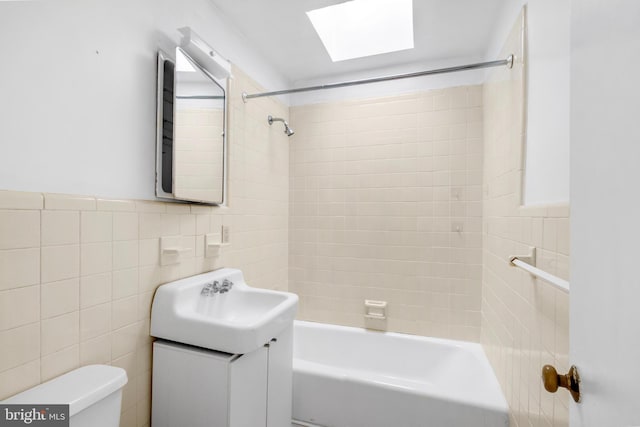 full bathroom with vanity, tiled shower / bath, a skylight, toilet, and tile walls