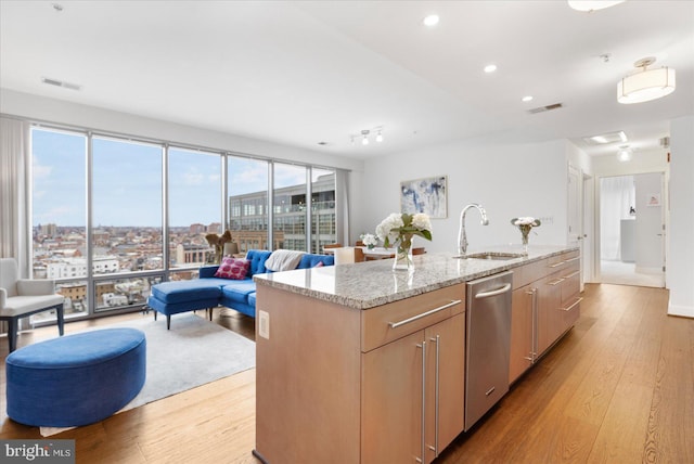 kitchen featuring light stone countertops, sink, dishwasher, light hardwood / wood-style floors, and a center island with sink