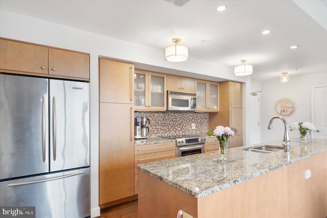 kitchen with backsplash, light stone counters, stainless steel appliances, sink, and light hardwood / wood-style flooring