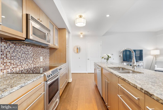 kitchen featuring sink, decorative backsplash, appliances with stainless steel finishes, light hardwood / wood-style floors, and light stone counters