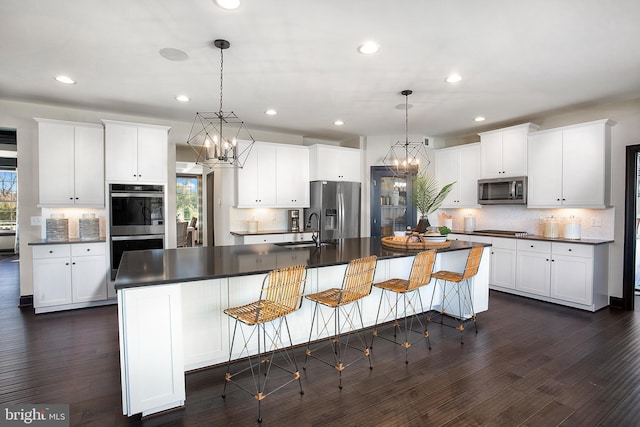 kitchen with dark wood-type flooring, stainless steel appliances, hanging light fixtures, and an island with sink