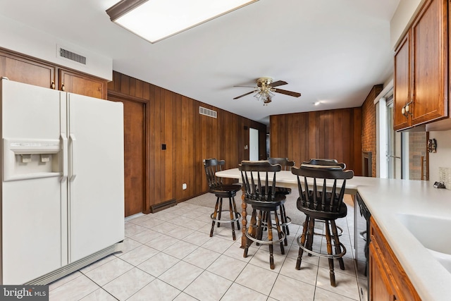 kitchen with ceiling fan, black dishwasher, white refrigerator with ice dispenser, wooden walls, and light tile patterned floors