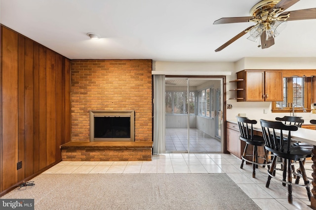 tiled living room with wood walls, ceiling fan, and a brick fireplace