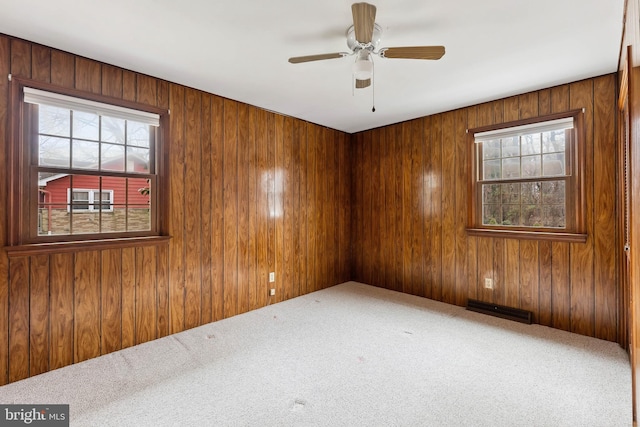 spare room featuring carpet flooring, wooden walls, and a wealth of natural light