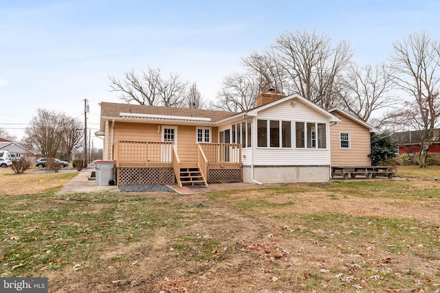 back of property with a sunroom, a deck, and a lawn