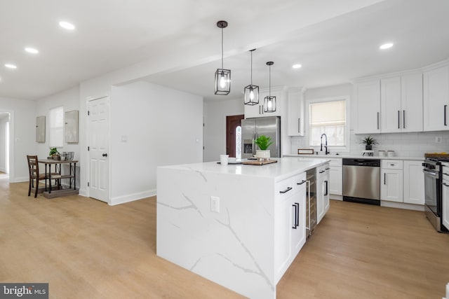 kitchen featuring light hardwood / wood-style floors, appliances with stainless steel finishes, decorative backsplash, white cabinets, and a center island