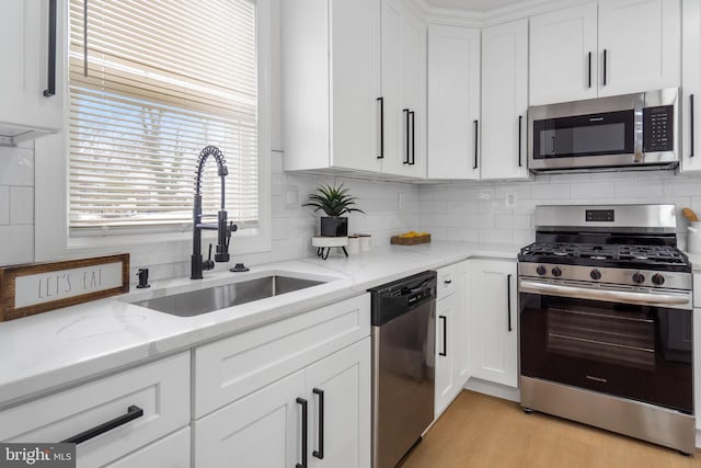 kitchen with backsplash, sink, stainless steel appliances, white cabinets, and light stone counters