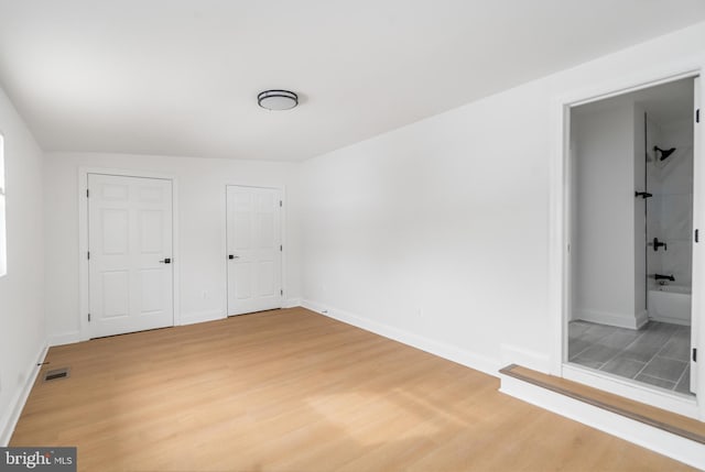 unfurnished bedroom with ensuite bath and hardwood / wood-style floors