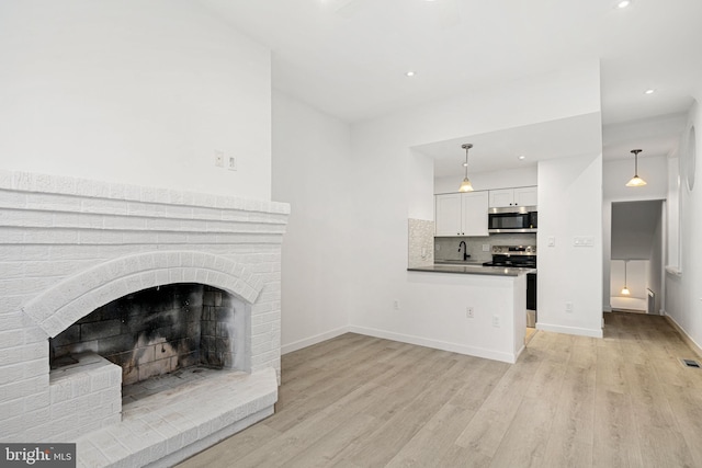 unfurnished living room featuring a brick fireplace, sink, and light wood-type flooring