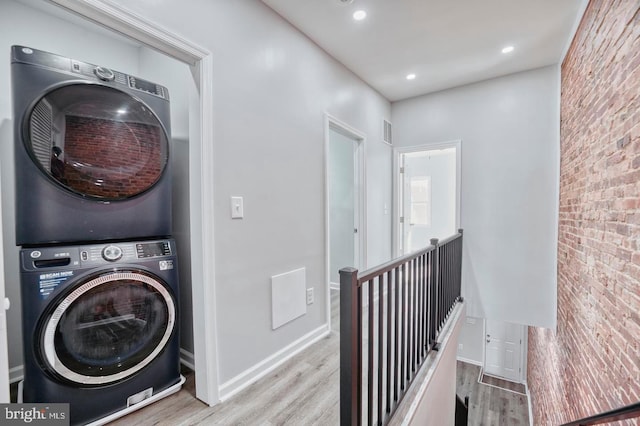 laundry area featuring stacked washer and dryer, brick wall, and light wood-type flooring