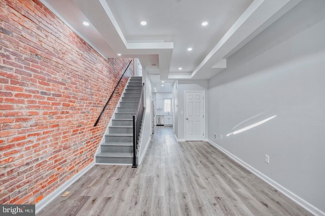 staircase with hardwood / wood-style floors, brick wall, and a tray ceiling