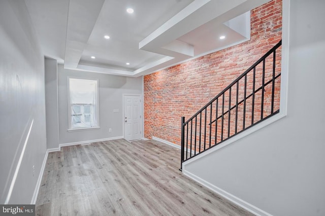 entryway with a raised ceiling, brick wall, and light hardwood / wood-style flooring