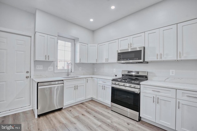 kitchen featuring light stone countertops, white cabinetry, sink, light hardwood / wood-style flooring, and appliances with stainless steel finishes