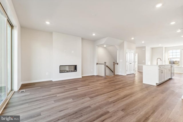 unfurnished living room featuring heating unit, light hardwood / wood-style flooring, and sink