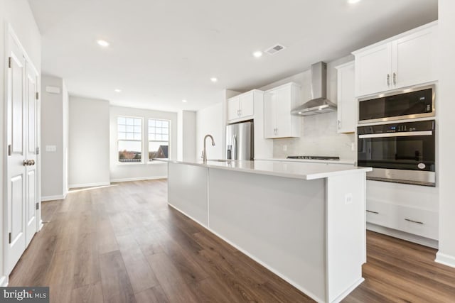 kitchen with white cabinetry, a center island with sink, wall chimney range hood, and appliances with stainless steel finishes