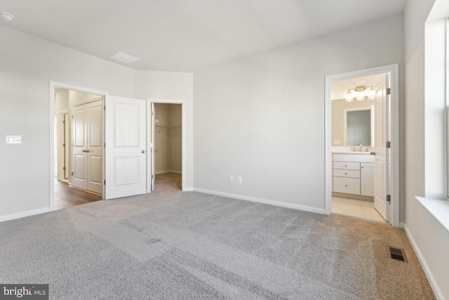 unfurnished bedroom featuring sink, a spacious closet, connected bathroom, light colored carpet, and a closet