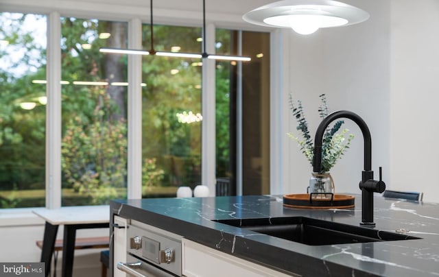 room details featuring dark stone countertops, white cabinetry, sink, and hanging light fixtures