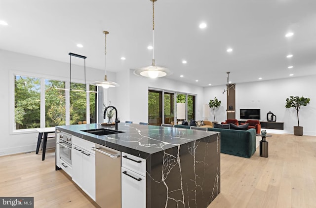 kitchen featuring white cabinetry, a healthy amount of sunlight, hanging light fixtures, dark stone counters, and a spacious island