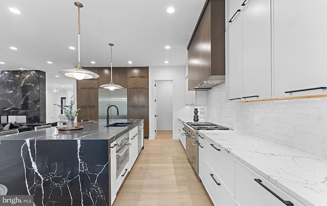 kitchen with white cabinetry, sink, wall chimney exhaust hood, hanging light fixtures, and light hardwood / wood-style floors