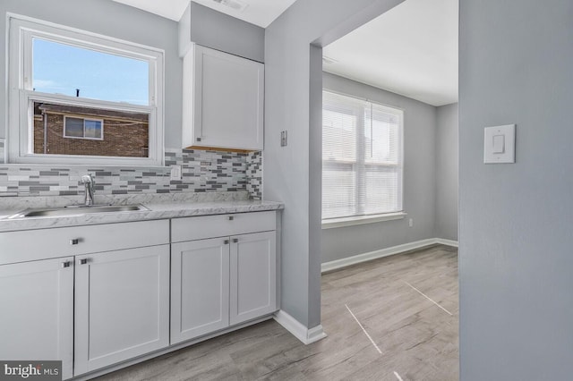 kitchen with backsplash, baseboards, white cabinets, and a sink